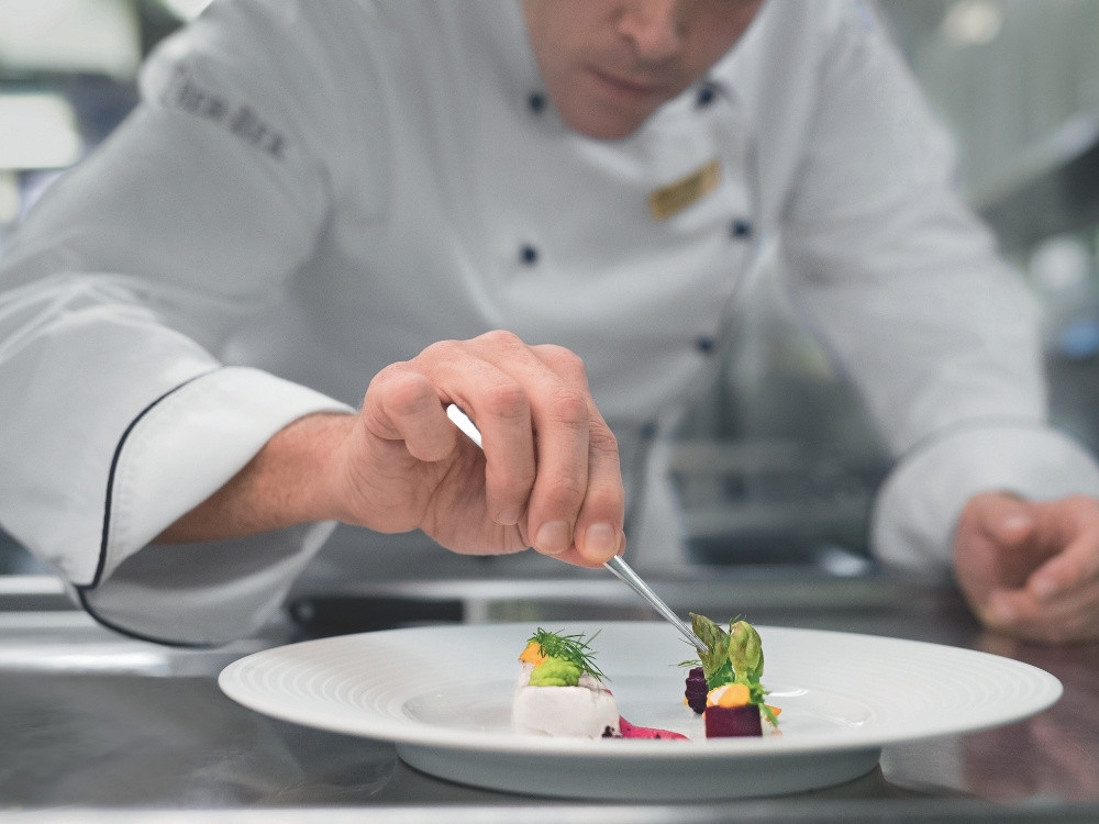 Koch richtet ein hochwertiges Gourmetgericht in der Küche der MS EUROPA mit großer Präzision an